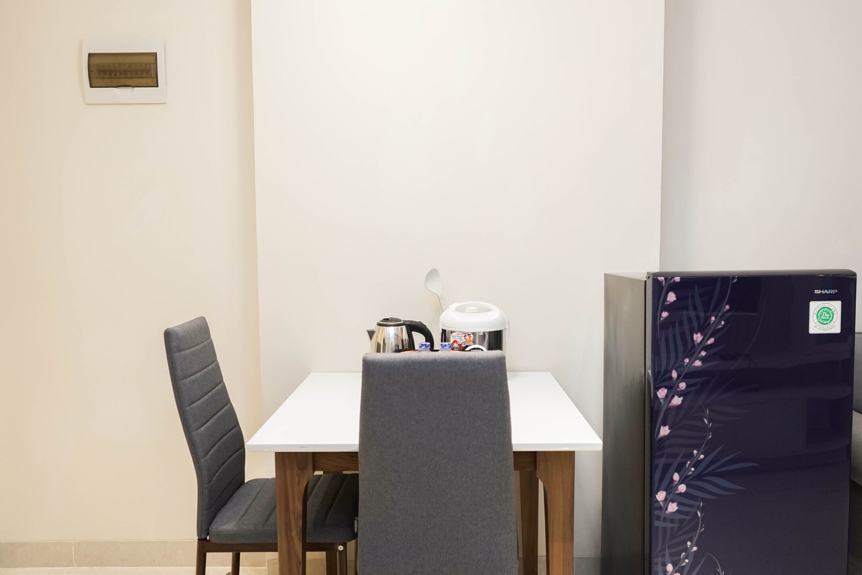 A small room with a white table, two chairs, a kettle, a coffee maker, and a refrigerator with a floral design.
