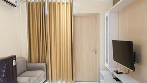 A modern living room with a sofa, a television mounted on the wall, and a door with a curtain. - 2BR Apartment at Elpis Residence near Ancol and Kemayoran (Jakarta)