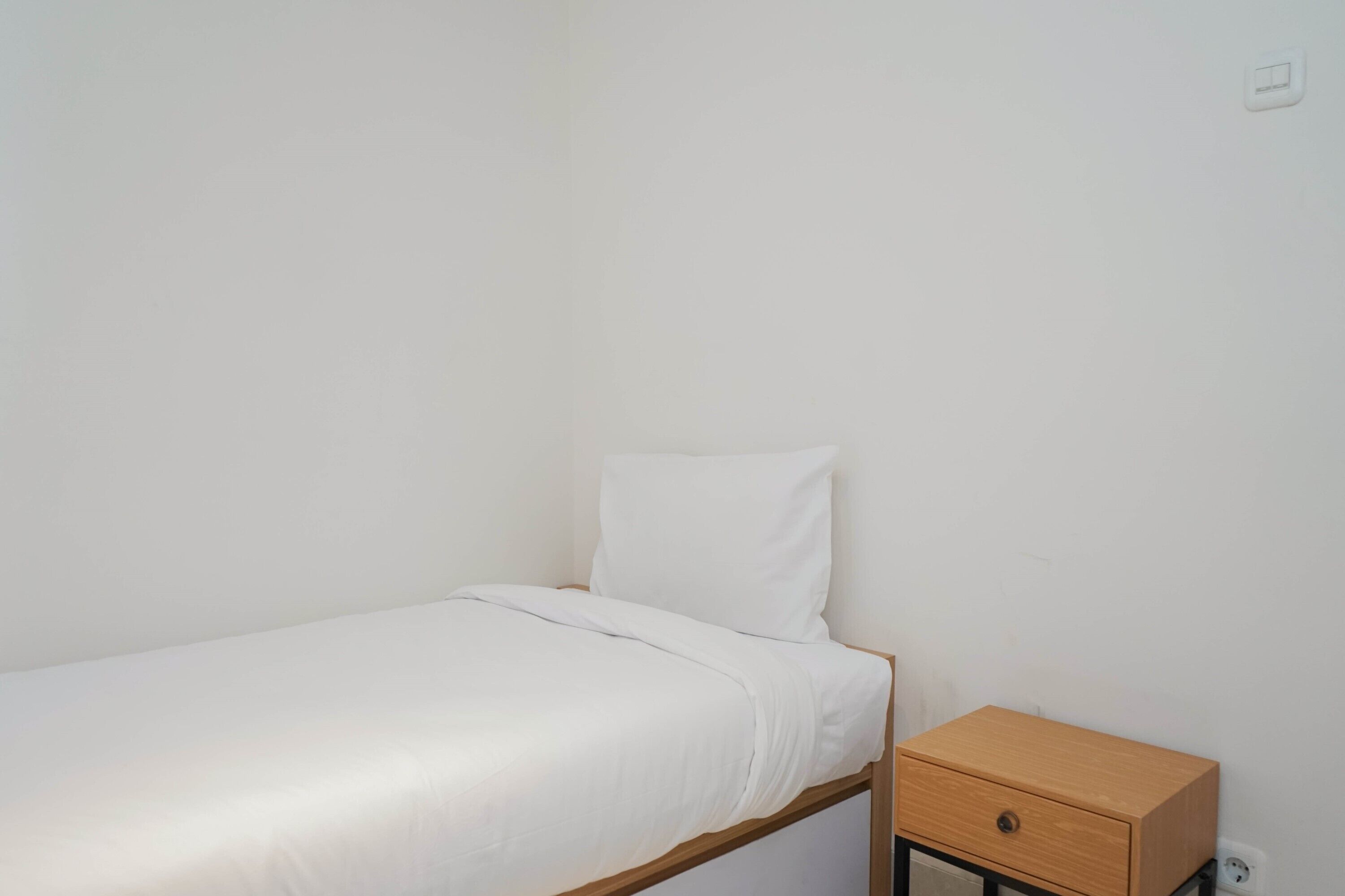Une petite chambre avec un lit simple, une table de chevet en bois et un tiroir.