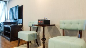 Habitación de hotel con un escritorio de madera, un televisor, dos sillones tapizados y una pequeña mesa redonda con un folleto turístico.