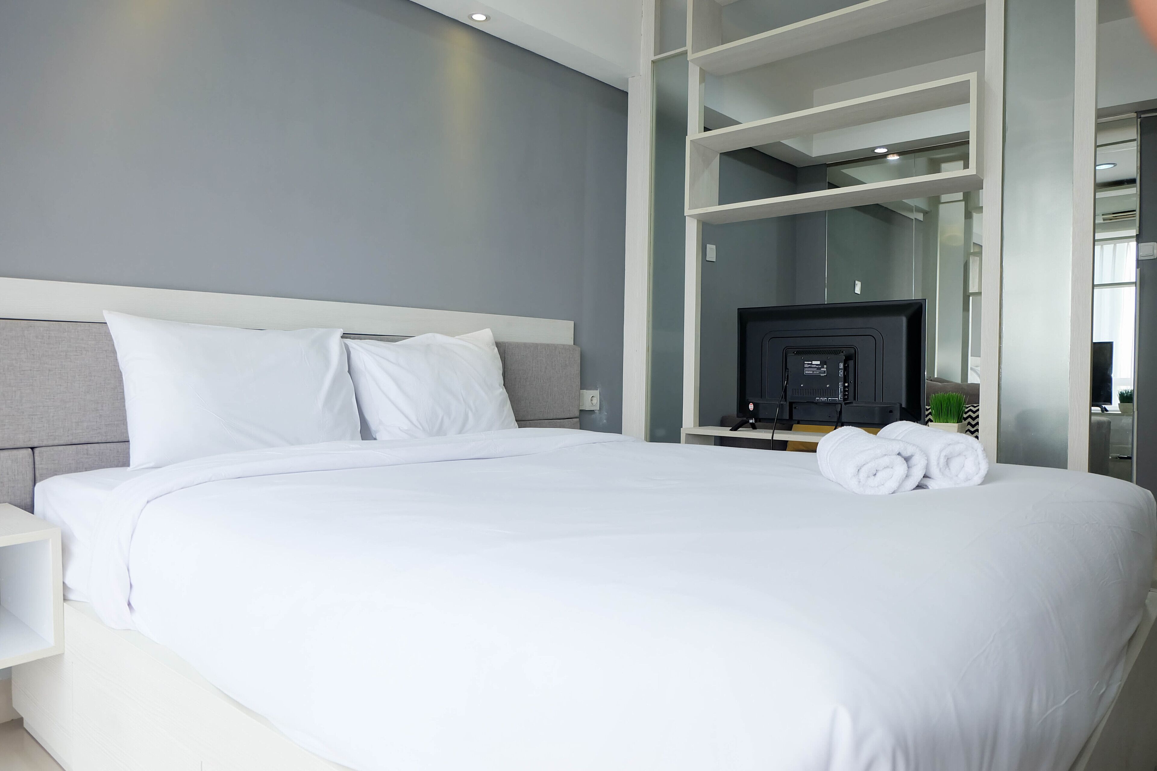 Ein modernes Hotelzimmer mit einem großen Bett, weißer Bettwäsche, einem Flachbildfernseher und einem Glaskastenbad.
