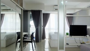 Habitación de hotel moderna con cama, escritorio, silla, televisor y balcón con cortinas.