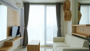 A modern living room with a flat-screen TV, a sofa, a coffee table, and wooden shelves. - Compact 1BR at Tree Park Apartment (South Tangerang)