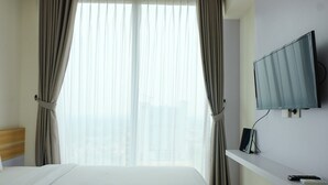 A hotel room with a bed, a TV mounted on the wall, and a window with curtains. - Compact 1BR at Tree Park Apartment (South Tangerang)