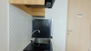 A compact kitchen with a built-in microwave, a sink, and a wooden cabinet above. - Compact 1BR at Tree Park Apartment (South Tangerang)