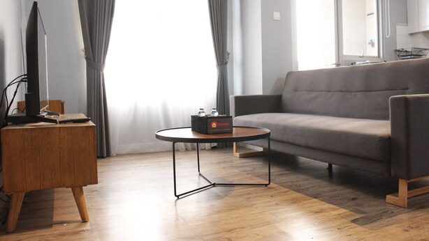 A modern living room with a grey sofa, a wooden coffee table, and a TV on a wooden stand. - Deluxe 2BR Apartment at Newton Residence with Mountain View (Bandung)