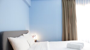 A neatly made bed with white linens, a grey headboard, and a bedside lamp with a crown-shaped light. - Deluxe 2BR Apartment at Newton Residence with Mountain View (Bandung)