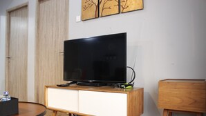 A modern living room with a flat-screen TV on a wooden cabinet, a round coffee table, and a small wooden side table. - Deluxe 2BR Apartment at Newton Residence with Mountain View (Bandung)
