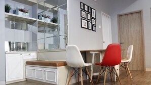 A modern kitchen with white cabinets, a wooden countertop, and a glass door leading to a balcony. There are two chairs, one white and one red, and a white dining table. - Deluxe 2BR Apartment at Newton Residence with Mountain View (Bandung)