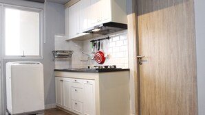 A compact kitchen with white cabinets, a built-in oven, and a wooden door. - Deluxe 2BR Apartment at Newton Residence with Mountain View (Bandung)