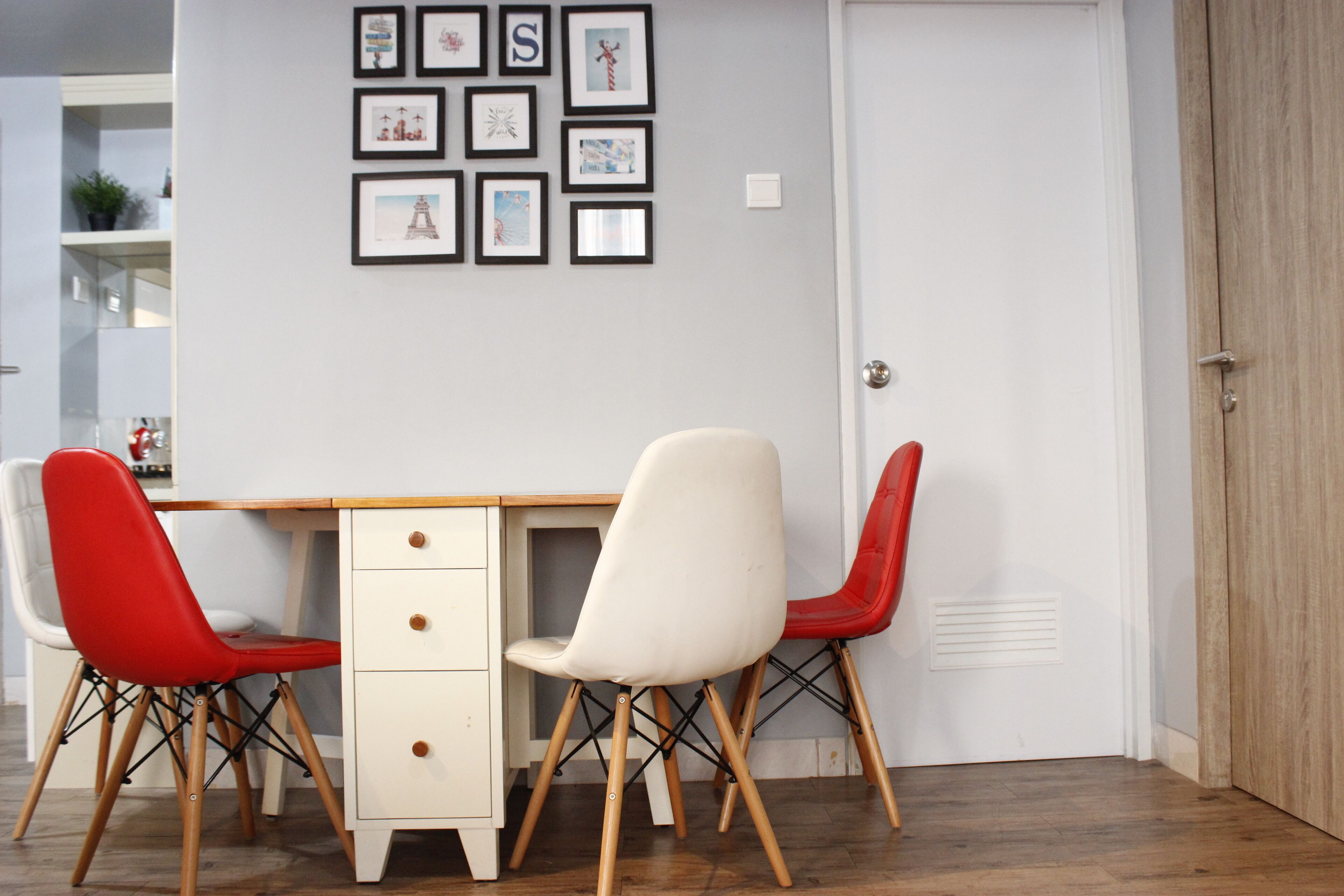 A dining area with a wooden table and two chairs, one red and one white, with a wall decorated with framed pictures.