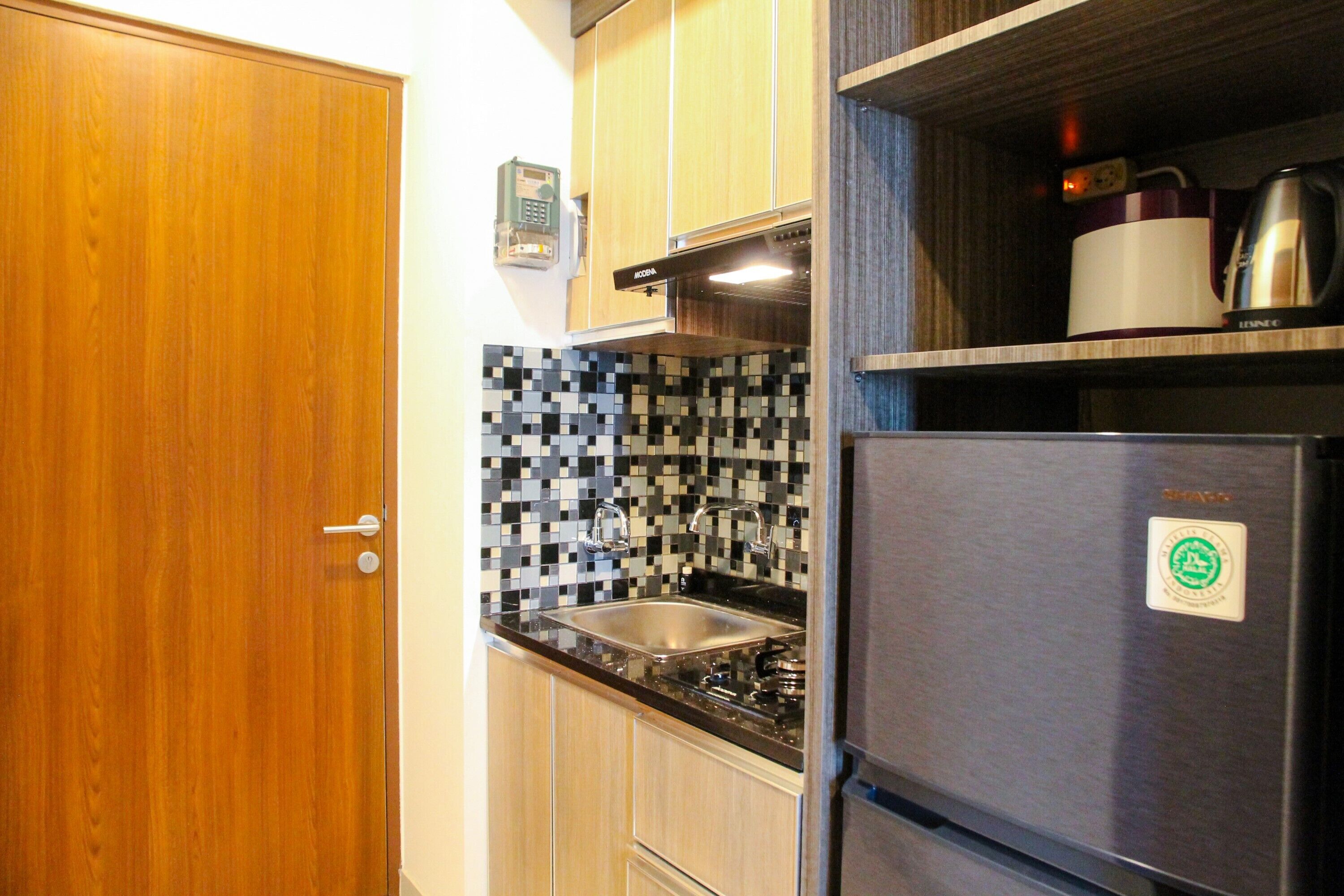 A kitchen with wooden cabinets, a black and white tiled backsplash, a stainless steel sink, and a refrigerator with a sticker.