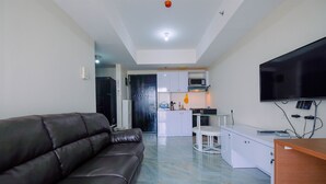 A modern living room with a leather sofa, a flat-screen TV, and a kitchen area with white cabinets and a microwave.