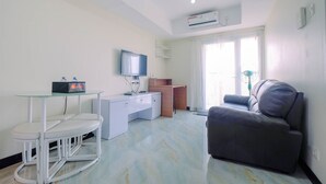 A modern living room with a flat-screen TV, a glass-top desk, a grey sofa, and a large window with curtains.