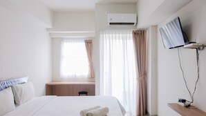 Une chambre d’hôtel équipée d’un lit, d’un bureau, d’un climatiseur, d’une télévision et de rideaux.