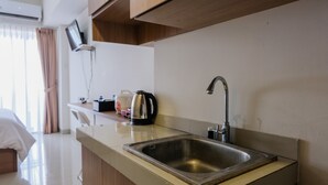 Une cuisine d’hôtel moderne, équipée d’un évier en acier inoxydable, d’une bouilloire et d’un téléviseur à écran plat fixé au mur.