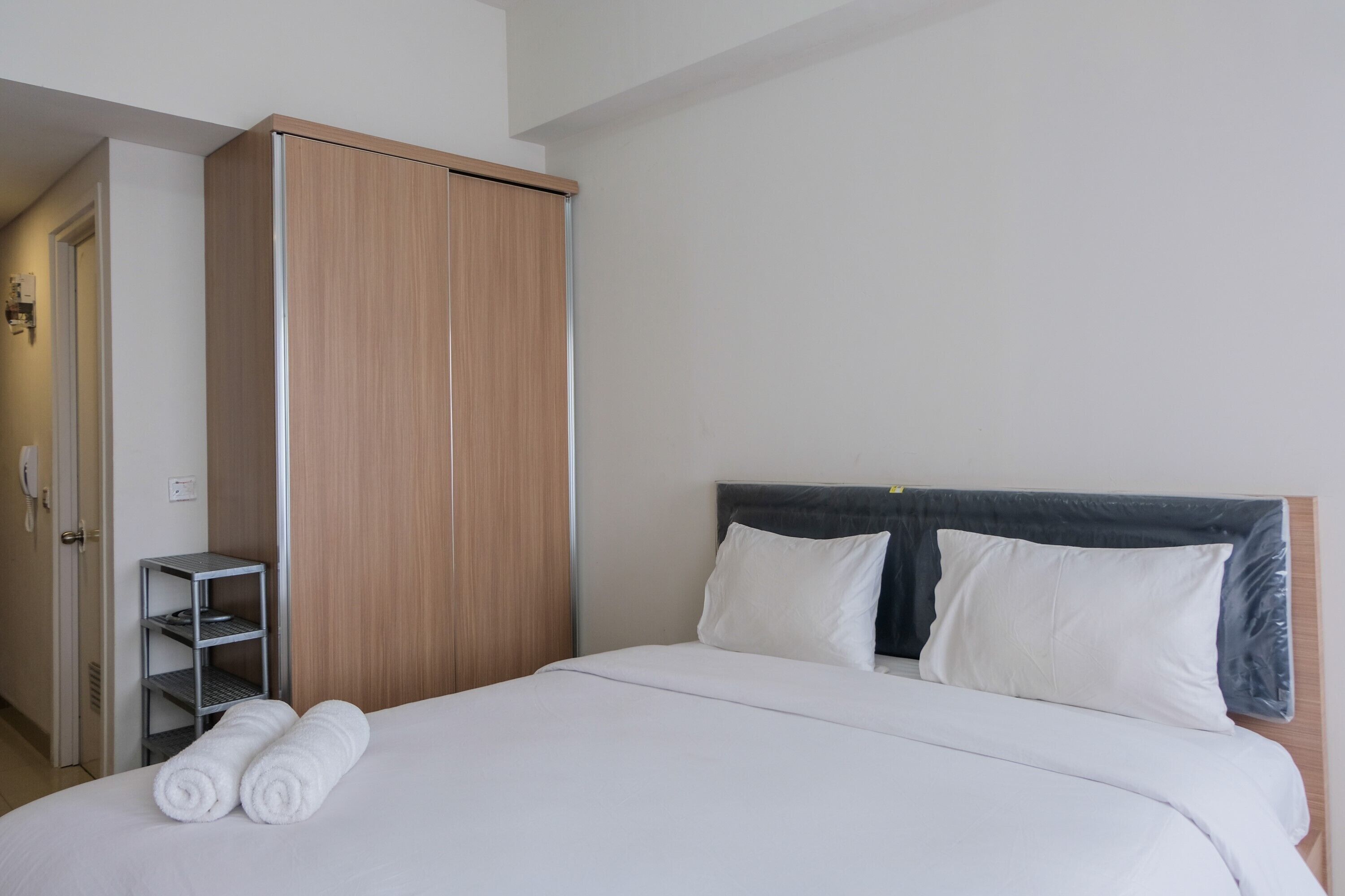 A hotel room with a bed, two pillows, a wooden wardrobe, and a metal shelf.