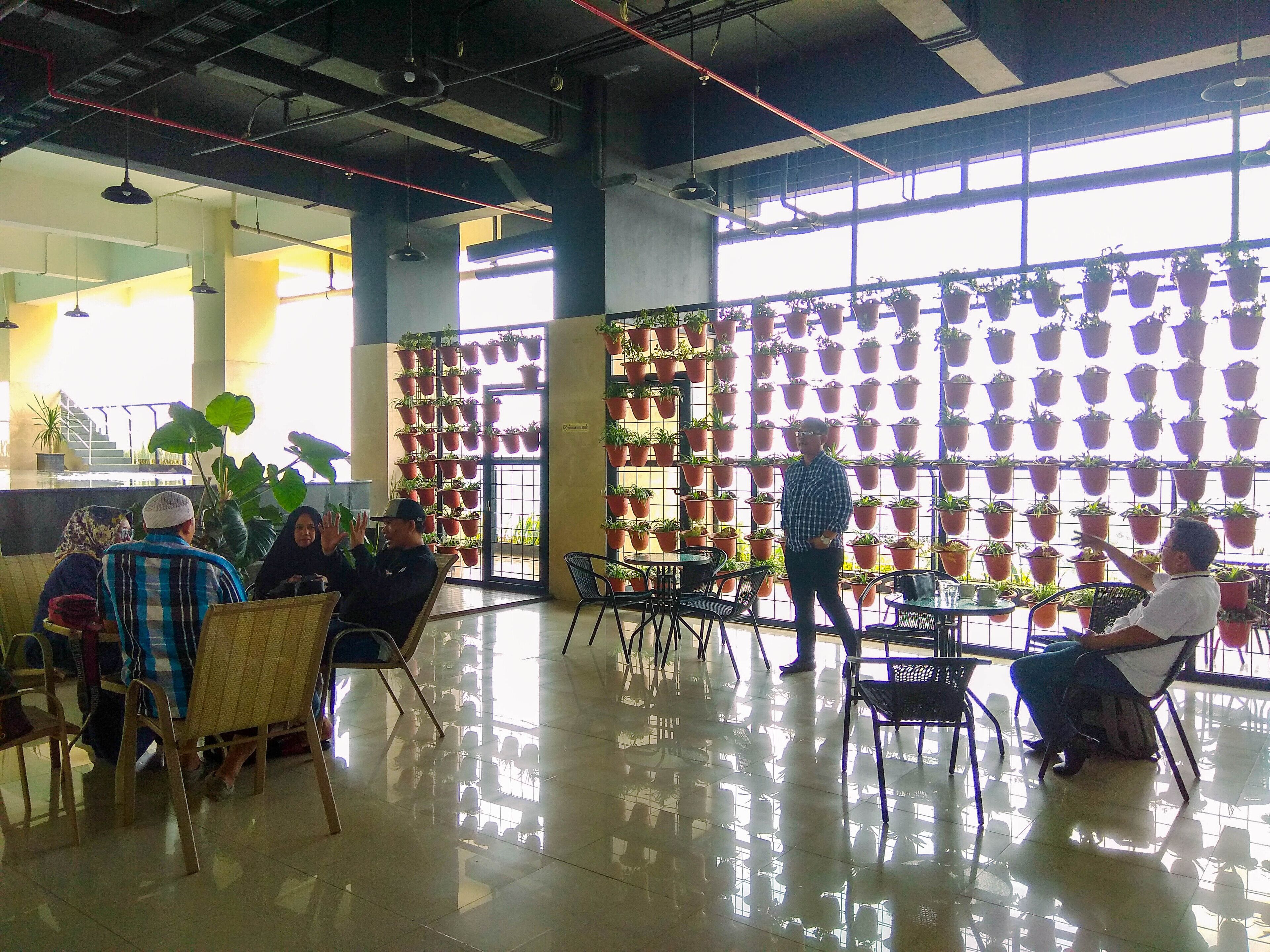 Un espacio interior amplio con techos altos, ventanas grandes y una pared con plantas colgantes en macetas.