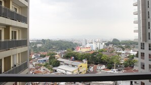 A high-rise building with multiple balconies, a view of a cityscape with various buildings and greenery, and a cloudy sky.