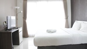 A hotel room with a bed, a desk with a television, and an air conditioning unit.