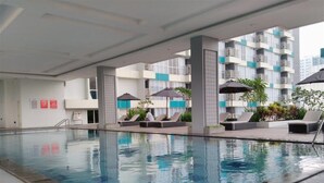 Una piscina con lettini e ombrelloni, circondata da un edificio a più piani con balconi.