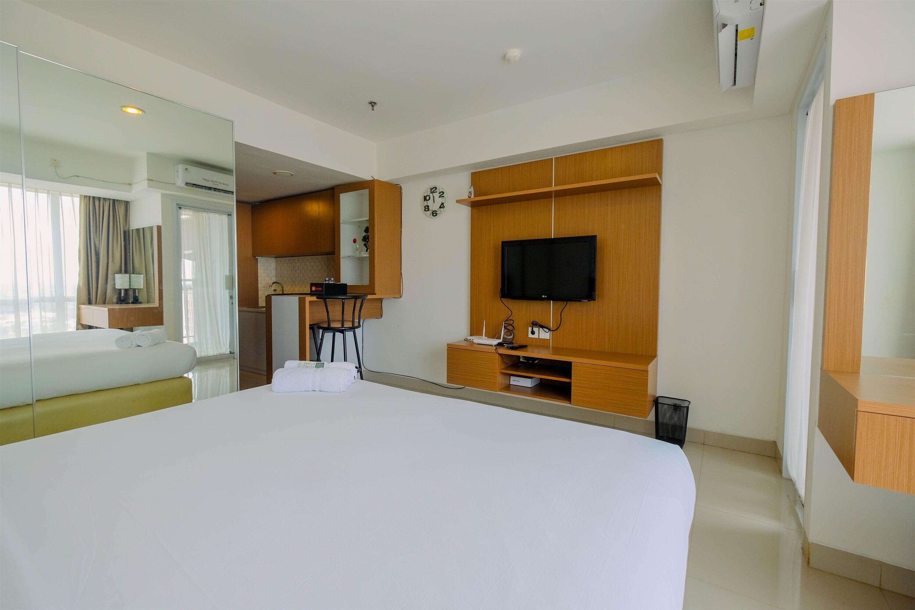 A hotel room with a large bed, a TV mounted on the wall, a small kitchenette, and a mirror.