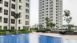 A swimming pool with a clear blue water surface, surrounded by a landscaped area with benches and a palm tree. - Elegant 2BR Apartment at M-Town Signature near Shopping Mall (Gading Serpong)