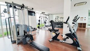 A modern gym with various exercise equipment, including weight machines, a bench, and cardio machines. - Elegant 2BR Apartment at M-Town Signature near Shopping Mall (Gading Serpong)