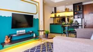 A modern living room with a flat-screen TV, a sofa, a coffee table, and a kitchen area with a bar. - Elegant 2BR Apartment at M-Town Signature near Shopping Mall (Gading Serpong)