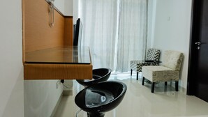 A modern room with a wooden cabinet, a black chair, a patterned armchair, and a door. - Modern and Cozy 1BR Brooklyn Alam Sutera Apartment (South Tangerang)