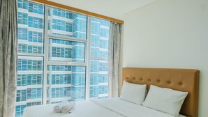 A hotel room with a large window, a bed with white linens, and a wooden headboard. - Modern and Cozy 1BR Brooklyn Alam Sutera Apartment (South Tangerang)