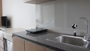 A modern kitchen with a granite countertop, stainless steel sink, and wooden cabinets. - Classic Studio Room Taman Melati Apartment Jatinangor near UNPAD (Hegarmanah)