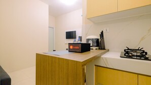 Une cuisine compacte avec un comptoir en bois, une machine à café de la marque Travelio, une cuisinière à gaz et un téléviseur fixé au mur.