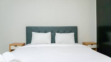 Un lit bien fait, avec du linge de lit blanc et des oreillers, une tête de lit capitonnée et deux tables de chevet en bois dotées de tiroirs.