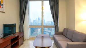 A modern living room with a sofa, a flat-screen TV on a wooden stand, a coffee table, and a large window with curtains. - Stunning 2BR at The Empyreal Condominium Epicentrum Apartment (Jakarta)