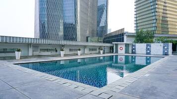 A swimming pool with a tiled edge, surrounded by a low wall and potted plants.