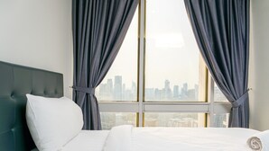 Quarto de hotel com uma cama grande, cortinas cinzas e vista para a cidade pela janela.