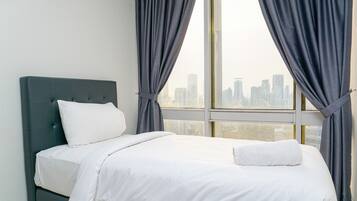 A neatly made bed with white linens and a dark headboard in a room with large windows and grey curtains.