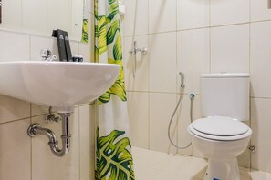 A bathroom with a white sink, a toilet, and a shower with a green leaf-patterned shower curtain. - Minimalist and Cozy Room 1BR Asatti Apartment (Pagedangan)