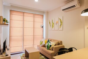 A modern living room with a sofa, a coffee table, a TV, and a dining table. - Minimalist and Cozy Room 1BR Asatti Apartment (Pagedangan)