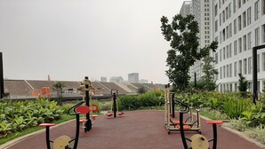 Un espace extérieur aménagé pour la pratique d’exercices physiques, équipé de matériel de remise en forme, entouré de verdure et avec des bâtiments en arrière-plan.