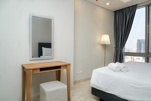 Ein Hotelzimmer mit Bett, Nachttisch, Hocker, Spiegel, Lampe und einem Fenster mit Vorhängen.