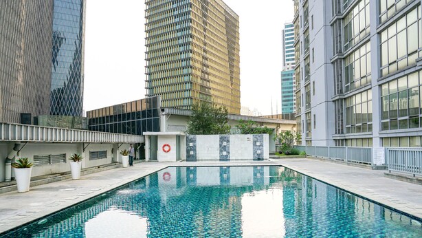 A swimming pool with a tiled pattern, surrounded by modern buildings and a white fence. - Cozy 2BR @ The Empyreal Condominium Epicentrum Apartment (Jakarta)