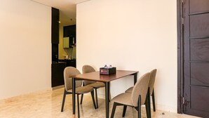 A dining area with a table and four chairs, a dark door, and a kitchen visible through an open doorway. - Cozy 2BR @ The Empyreal Condominium Epicentrum Apartment (Jakarta)