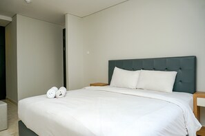 A neatly made bed with white linens and two rolled towels, a dark upholstered headboard, and a wooden nightstand with a drawer. - Cozy 2BR @ The Empyreal Condominium Epicentrum Apartment (Jakarta)