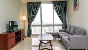 A modern living room with a grey sofa, a wooden TV stand, and a large window with curtains. - Cozy 2BR @ The Empyreal Condominium Epicentrum Apartment (Jakarta)