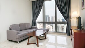 A modern living room with a grey sofa, a wooden coffee table, and a large window with curtains. - Luxury 2BR at The Empyreal Condominium Epicentrum Apartment (Jakarta)