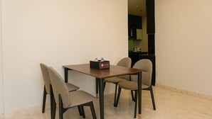 A dining area with a table and four chairs, a black box with a logo on the table, and a kitchen visible in the background. - Luxury 2BR at The Empyreal Condominium Epicentrum Apartment (Jakarta)