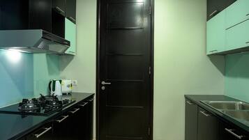 A compact kitchen with a black door, stainless steel appliances, and teal cabinets.