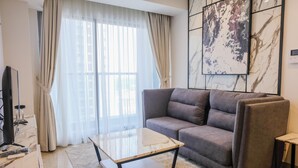 A modern living room with a grey sofa, a glass coffee table, and a large window with sheer curtains.
